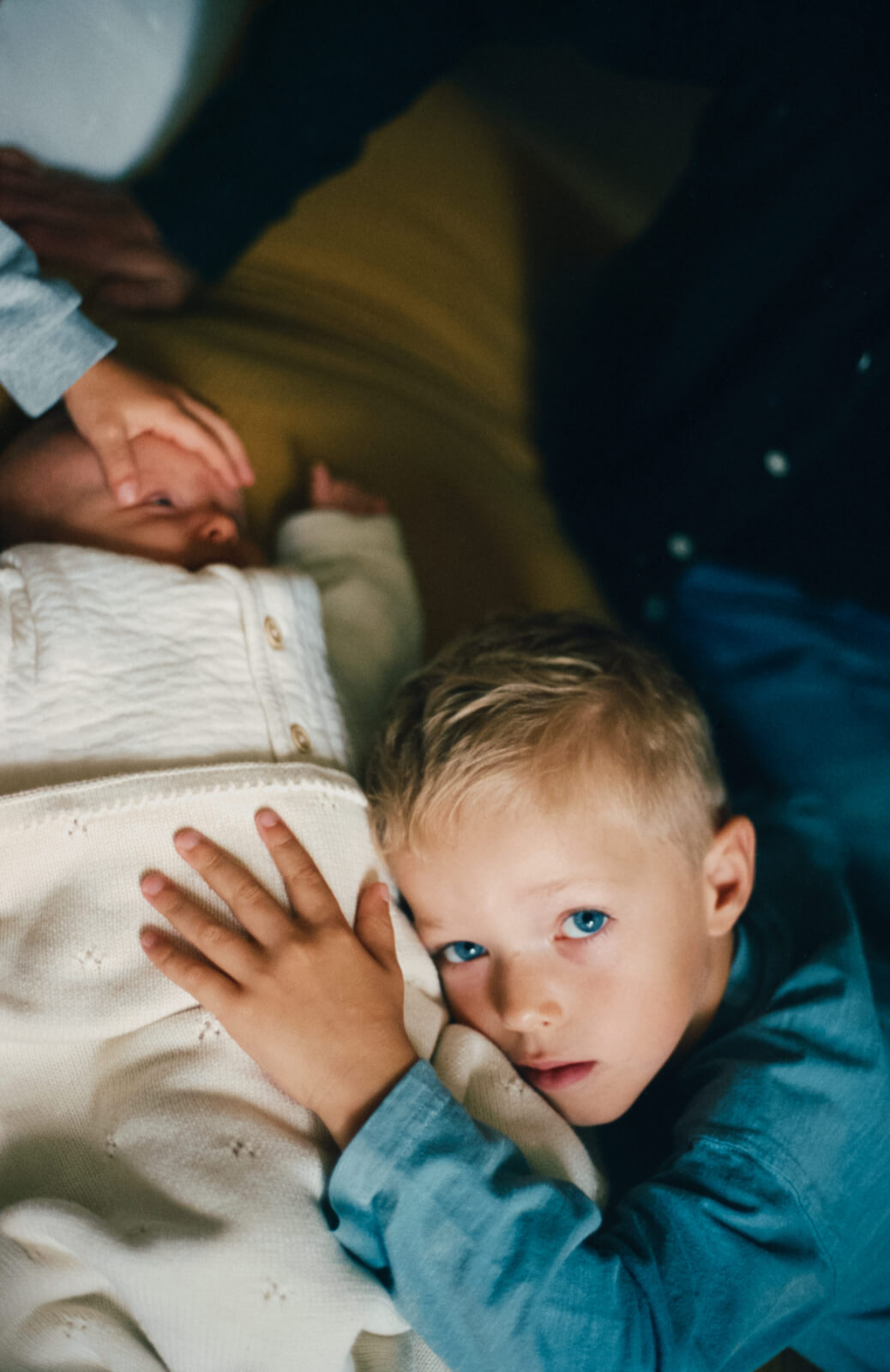 un enfant, la main sur sa petite soeur bébé, regarde vers la camera 