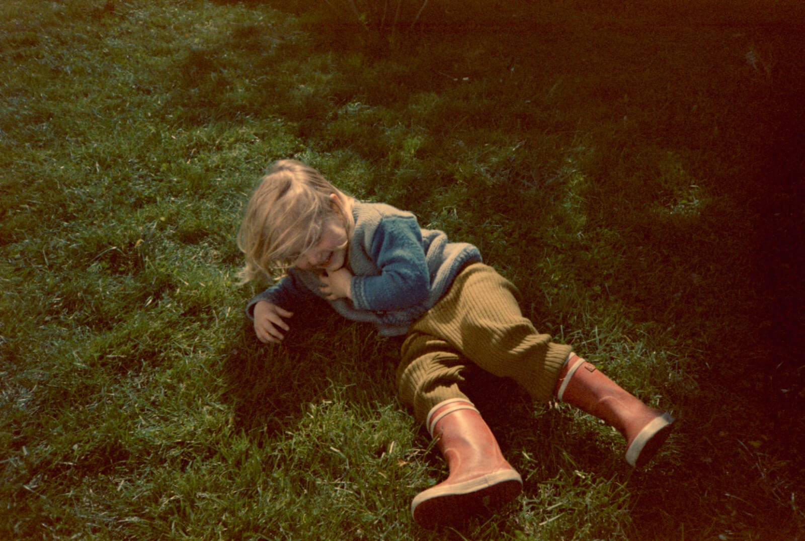 un enfant rit et joue à rouler dans l'herbe du jardin