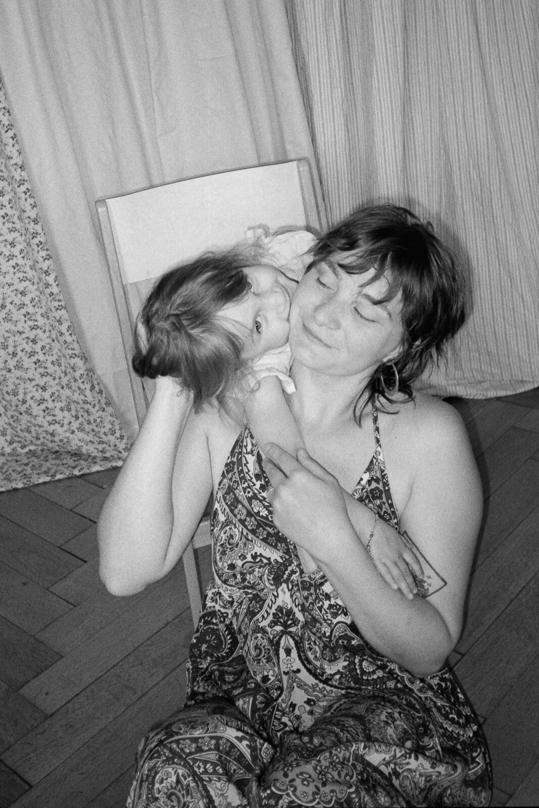 une maman assise au sol avec sa fille qui lui fait un câlin autour du cou lors d'une séance photo pour la fête des mères