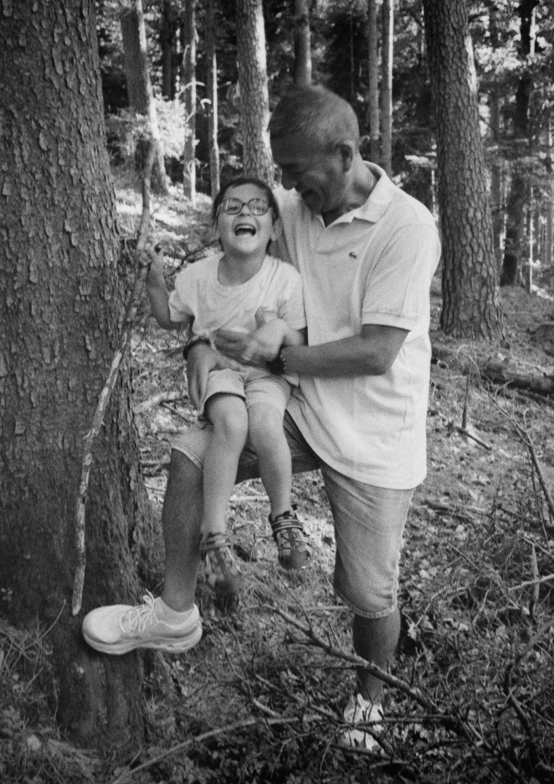 un père et son fils rient ensemble lors d'une séance photo argentique famille en forêt